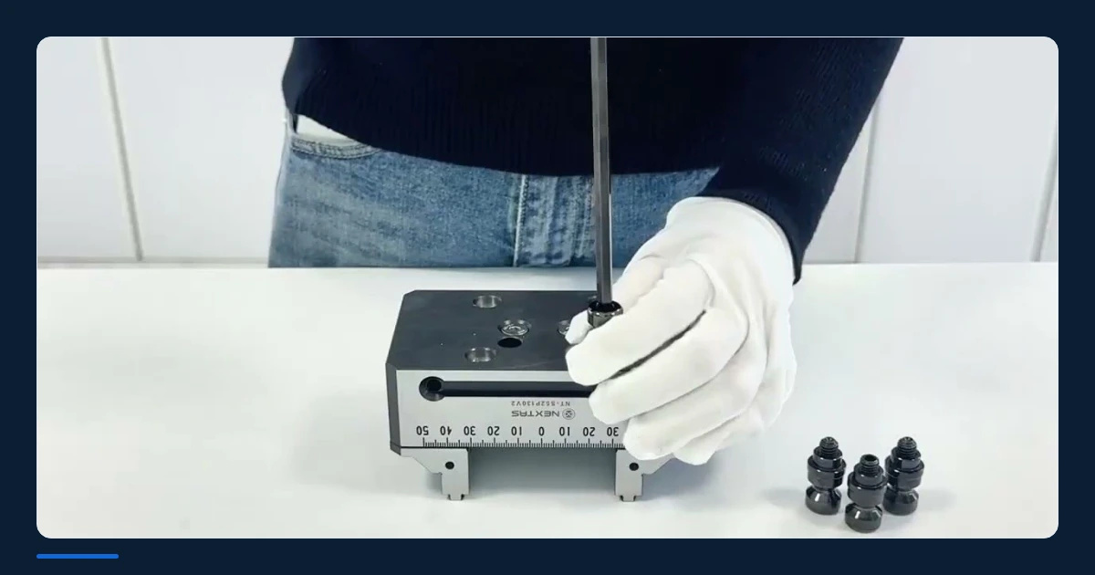 Gloved hands fitting a component to a self-centering vise on a workbench.