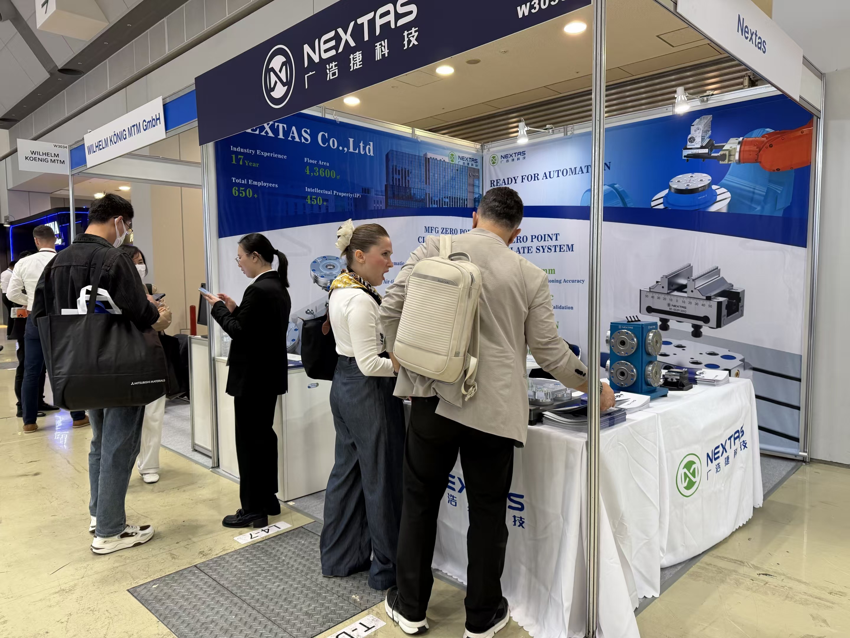 Visitantes en el estand de NEXTAS con el fondo READY FOR AUTOMATION y el rótulo W3035